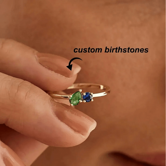 Gold ring with green and blue gemstones on a finger, labeled 'custom birthstones'.